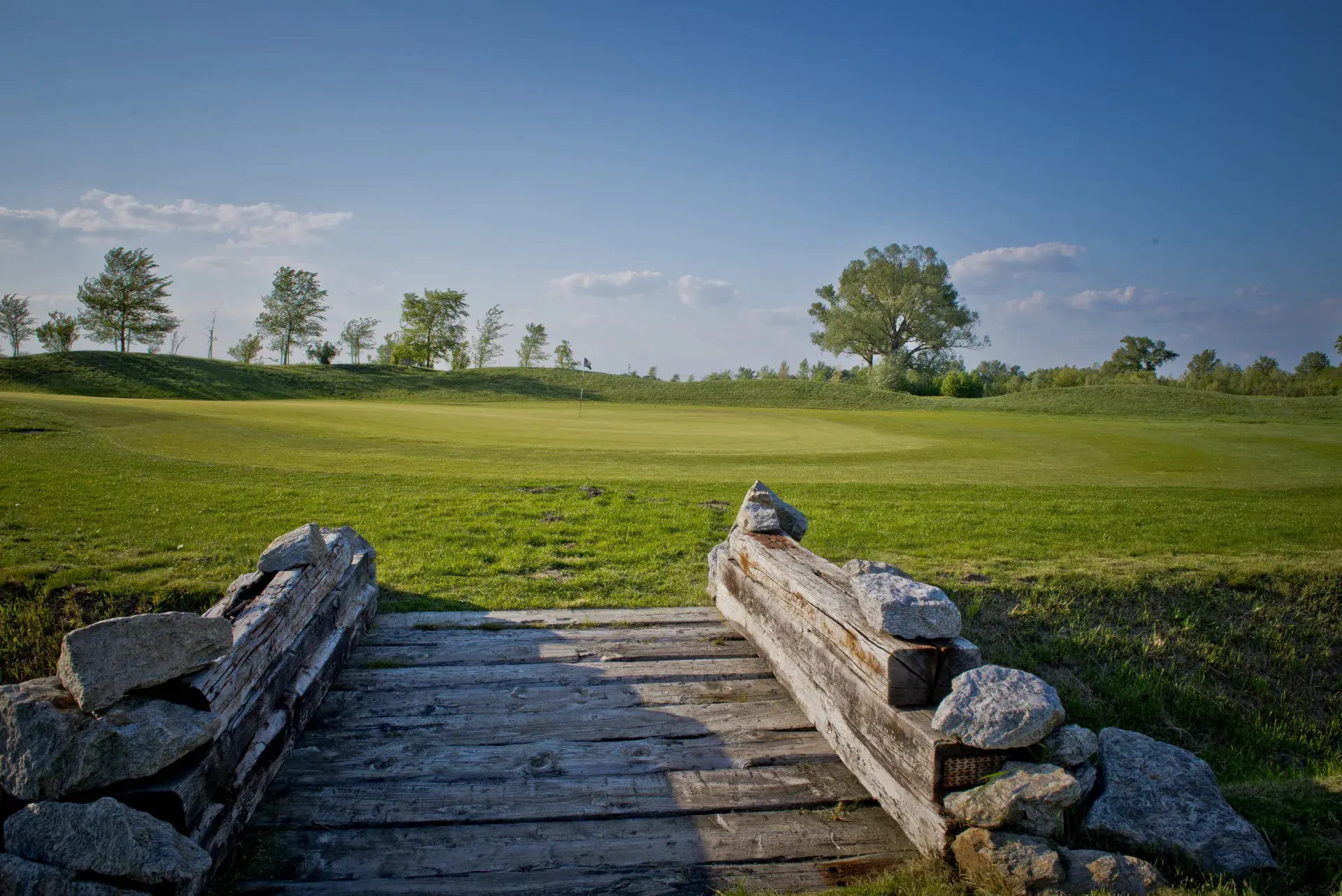 Gold Course green beyond a timber and stone bridge