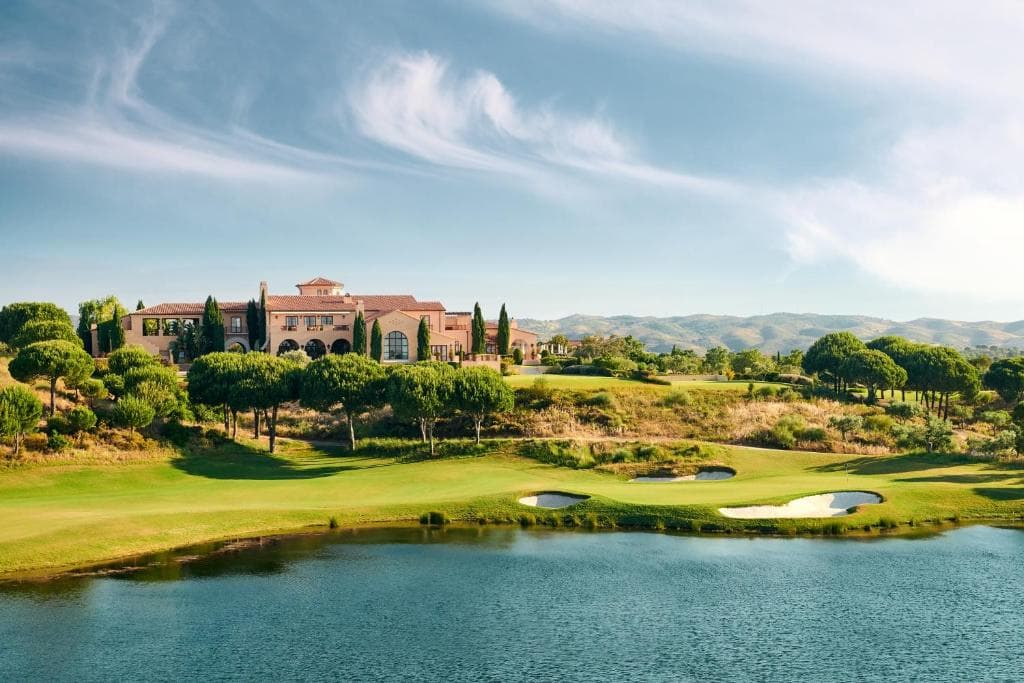 Green and bunkers beside a lake with the Monte Rei clubhouse beyond