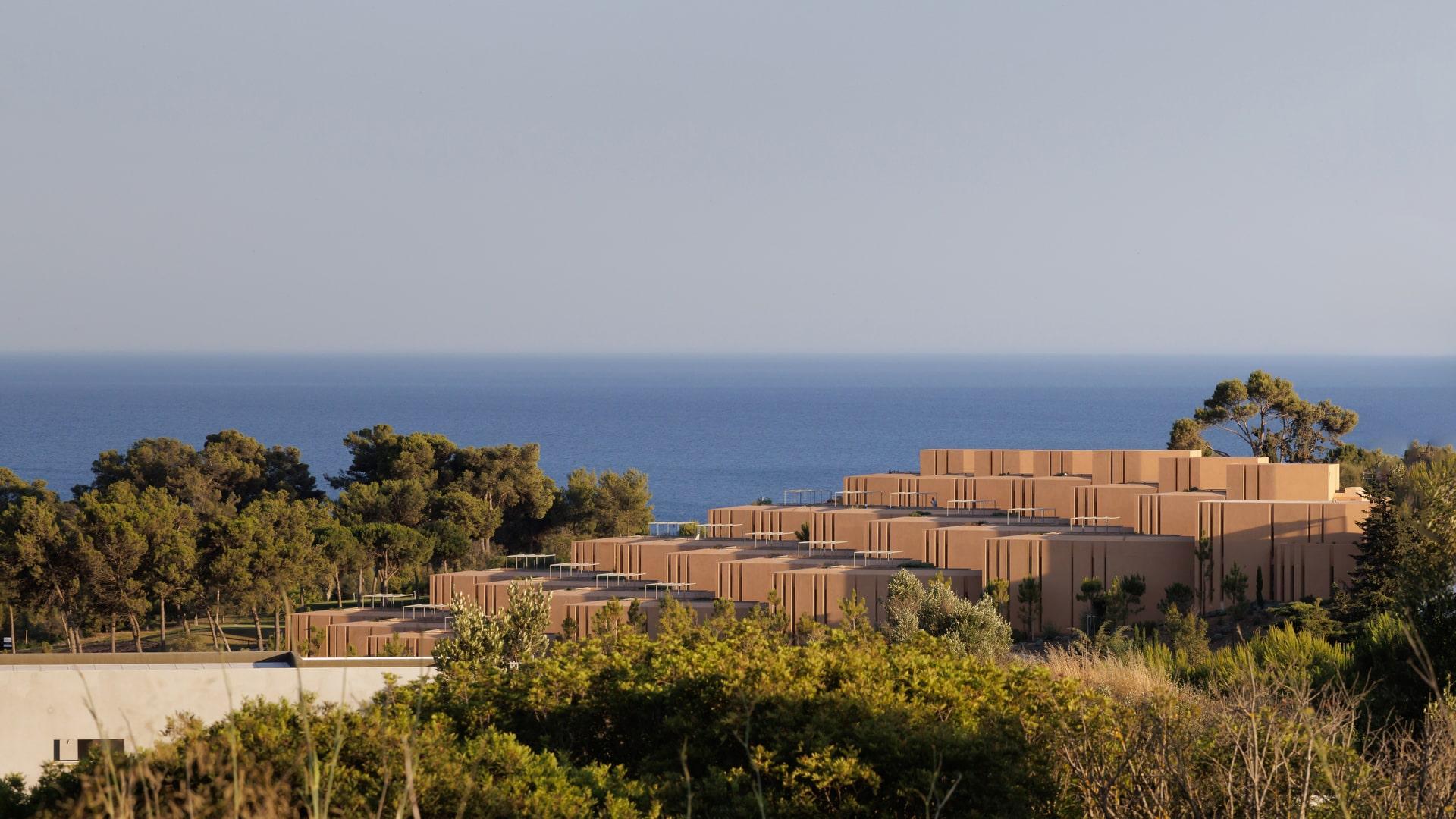 Terraced ochre apartment buildings among pines with the sea behind