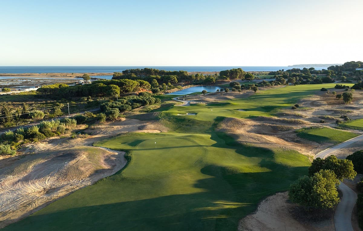Aerial view of a green and pond on the Palmares course with the estuary and sea beyond