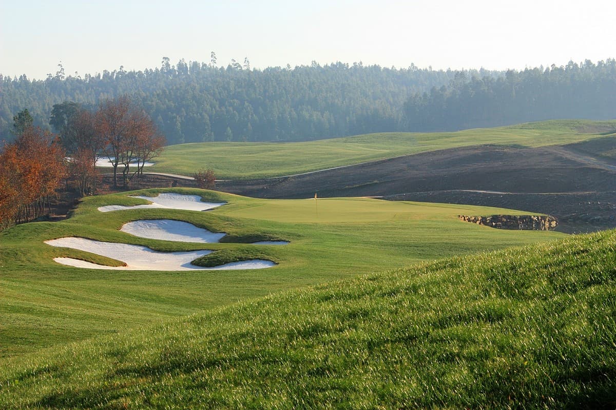 Green with sculpted bunkers in a wooded valley at Vale Pisão